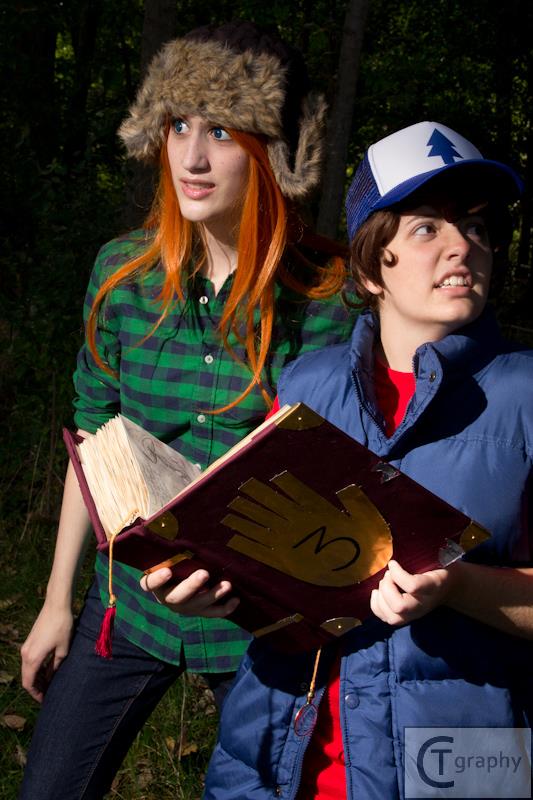 Two cosplayers. Wendy is on the left while Dipper is on the right holding up the Journal 3. Both looking nervously around.