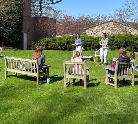 Two librarians act out a silly song with kids and their caregivers during an storytime on a sunny day in the library's garden space.