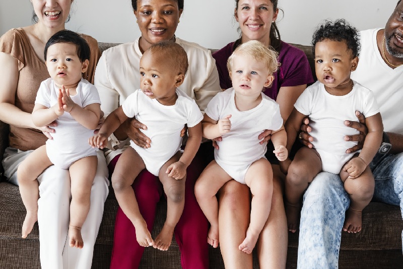 Multicultural babies sit on the laps of their caregivers.