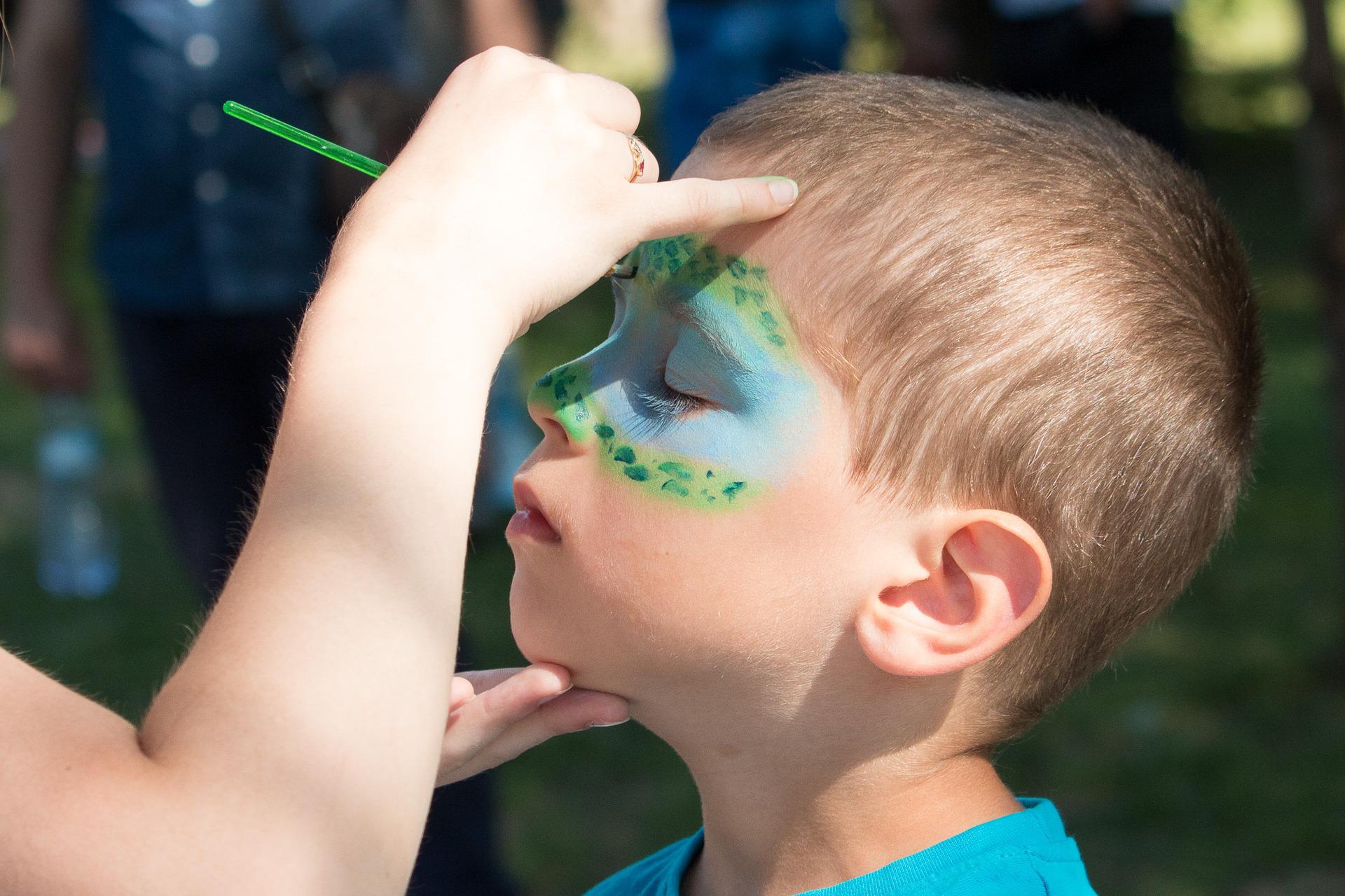 Child gets their face painted with blue and green face paint.
