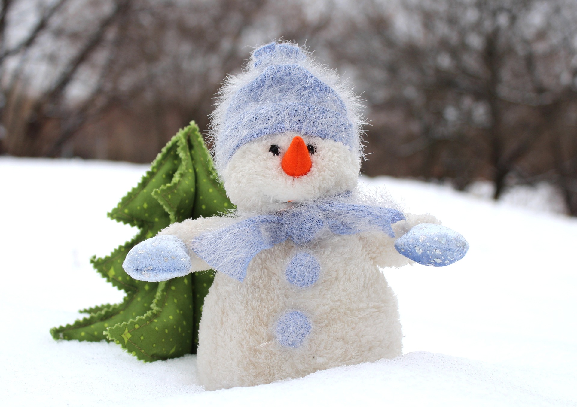 A fluffy snowman sits beside a felted tree on a winter landscape