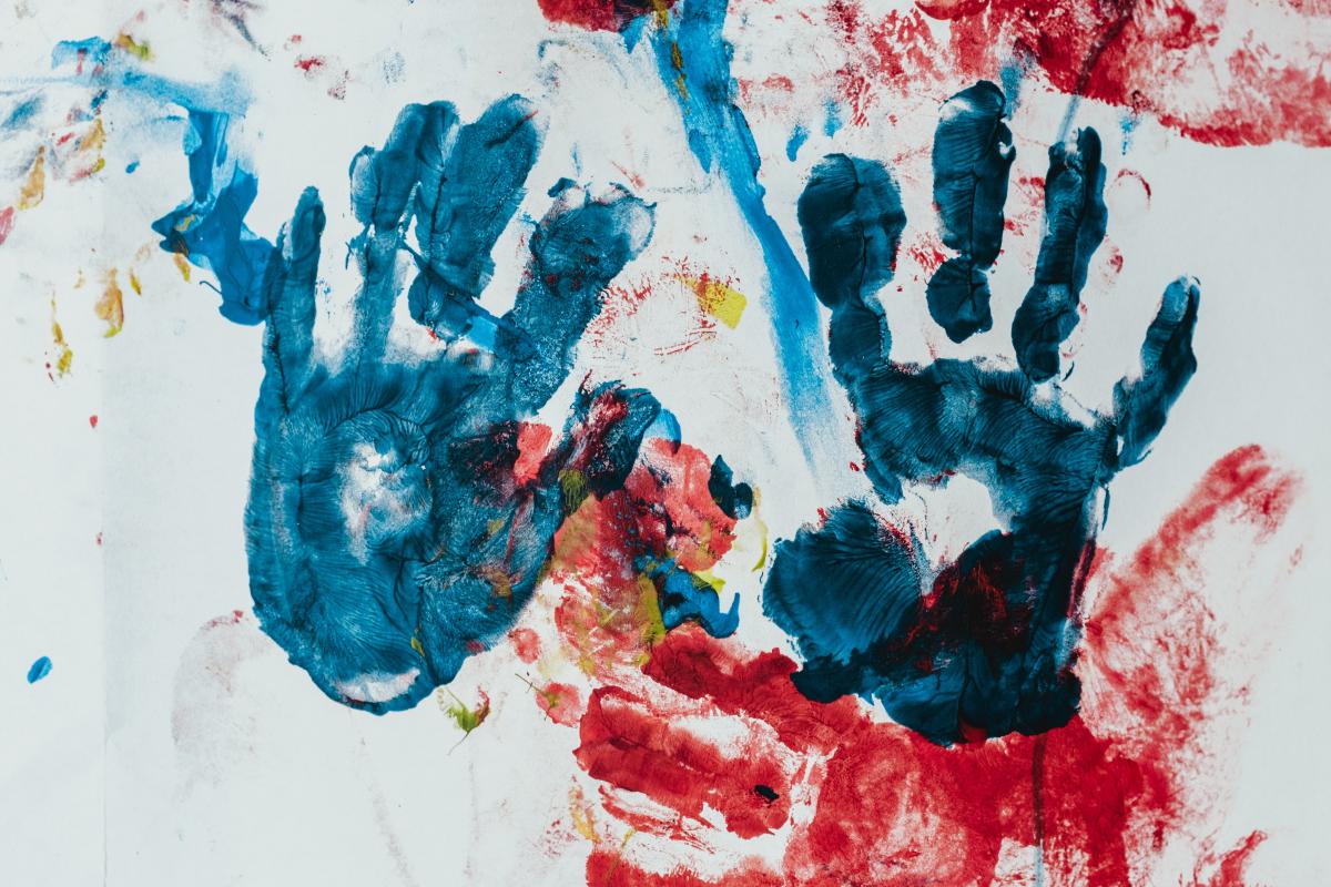 A white background with handprints in blue and red paint and paint drips.