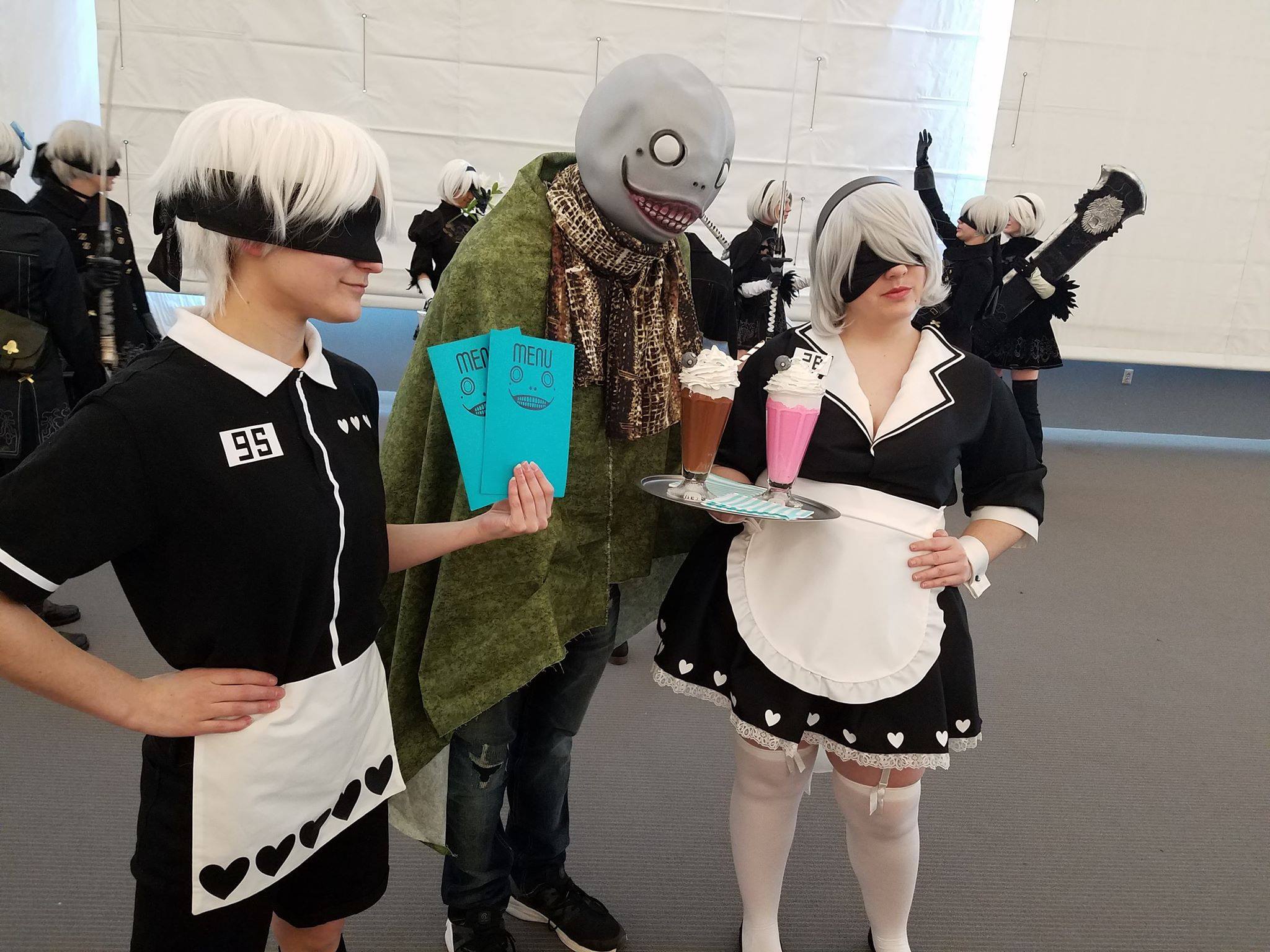 Three people cosplaying 2B, 9S, and Emil pose for a picture at an Anime Convention