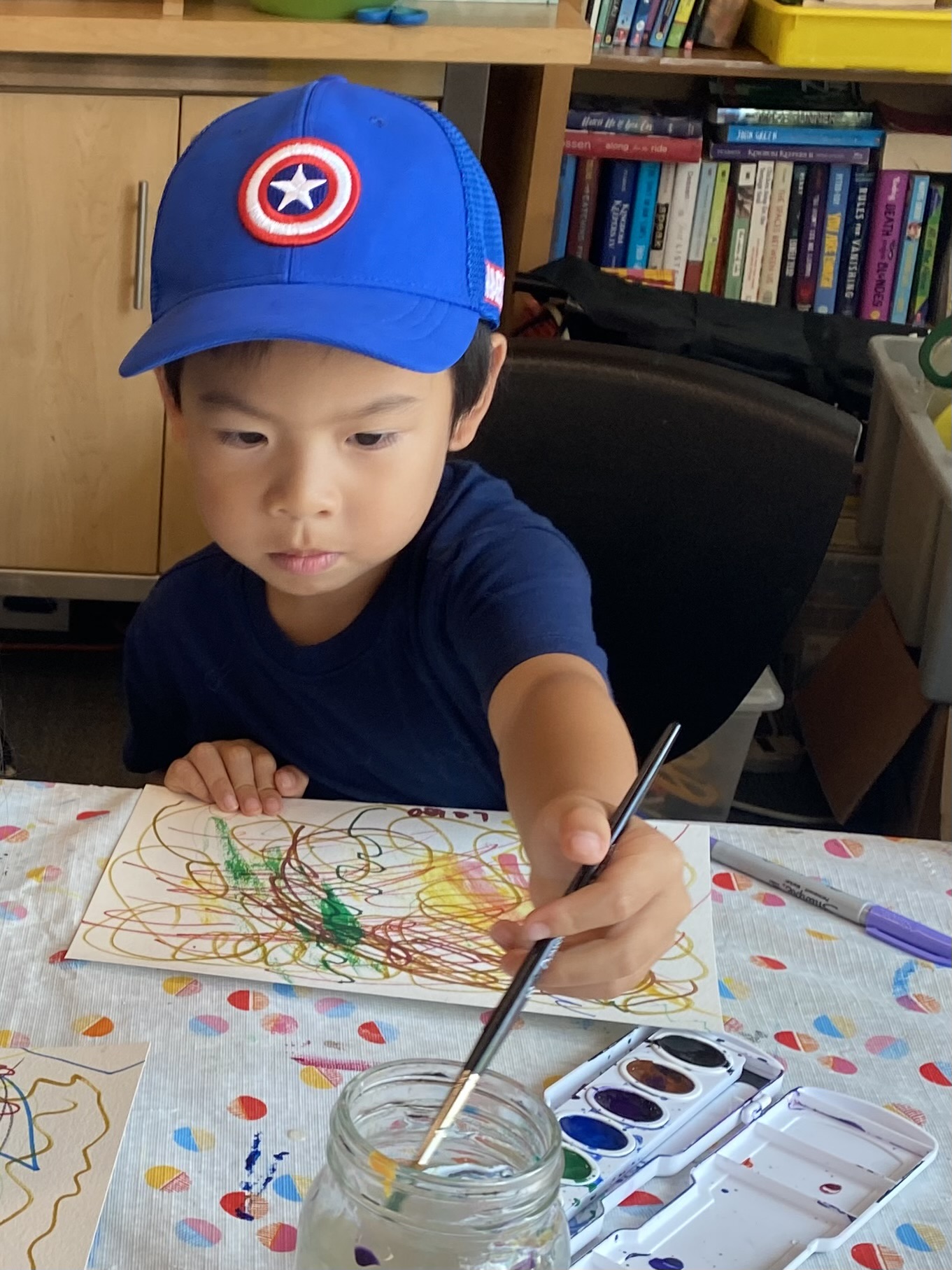 A preschool age boy in a blue baseball cap paints
