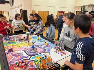 Group of teens in front of a game board work on programming LEGO robot.