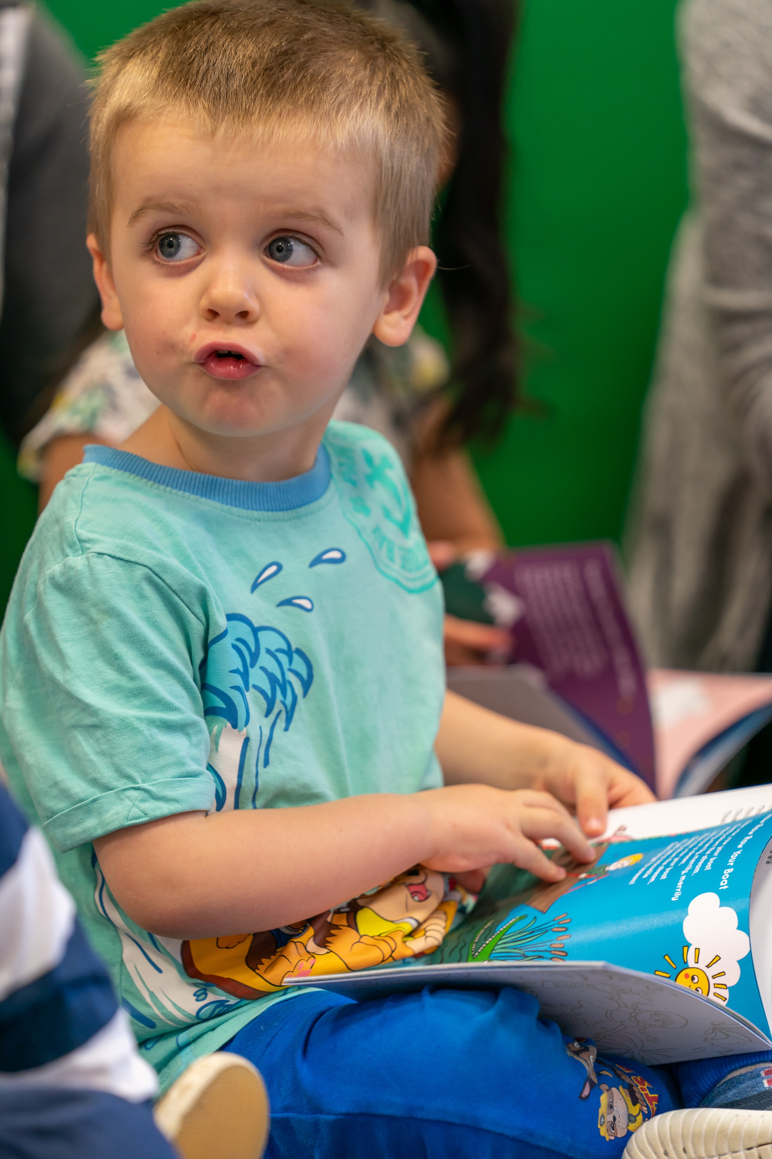 Toddler reading a book and making a funny face.