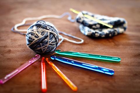 Multi-colored crochet hooks around a ball of yarn and a half-completed yarn project.