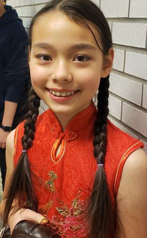 Local middle school student Rebecca is wearing a red outfit with gold embroidery and smiling.