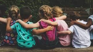 Multicultural group of children sit with their arms around each other.