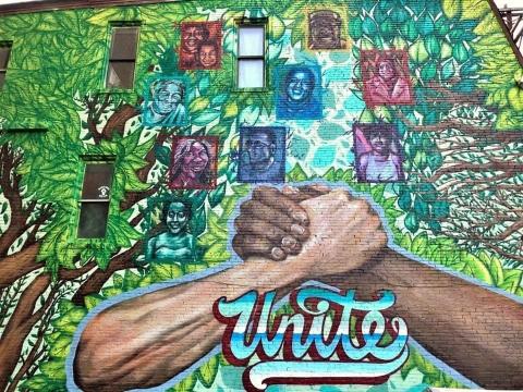 Photo of "Unite" mural on Main Street, Sharpsburg depicting Black and white hands grasping each other in foreground. Background is notable Sharpsburg residents.
