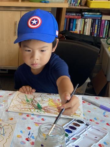 A preschool age boy in a blue baseball cap paints