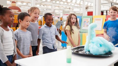 A group of kids watch a science experiment with amazed faces.