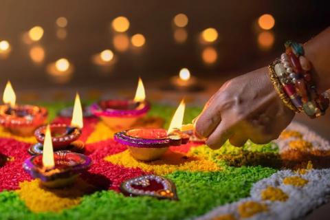 A hand lights lamps in a colorful sand rangoli