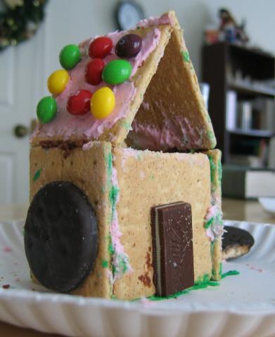 Photo of "gingerbread" house made of graham crackers, candy, chocolate, and icing.