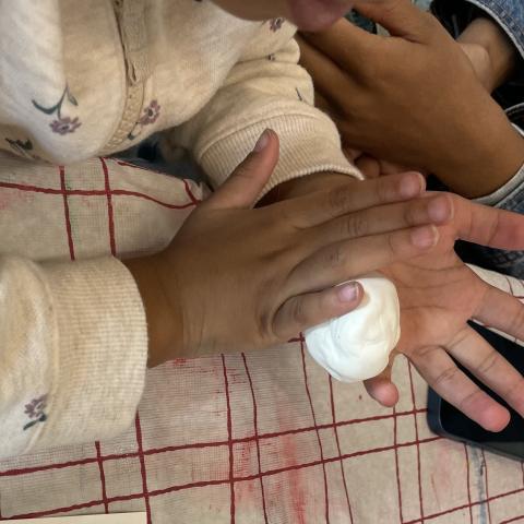 a child's hands roll a ball of clay with their grown up's hands visible next to them