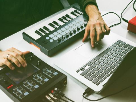 Photo of hands using keyboard, laptop, and recording equipment.