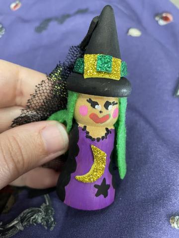 Photo of a wooden witch painted to wear a purple dress with moon & stars, a black hat, and green hair