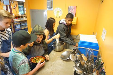 A group of multicultural teens prepare food in a kitchen