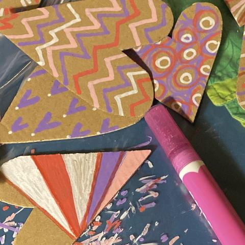 a paint marker sits on the table next to cardboard hearts colored with red and pink patterns.