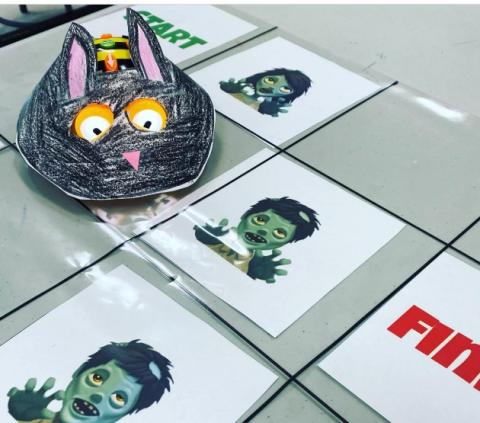A Bee Bot is wearing a paper, black cat costume and navigating a game board with vampires.