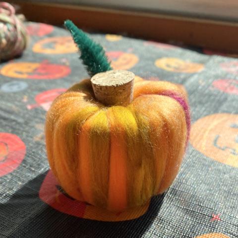 A photograph of a small pumpkin crafted out of wool roving, a pool noodle and a cork.