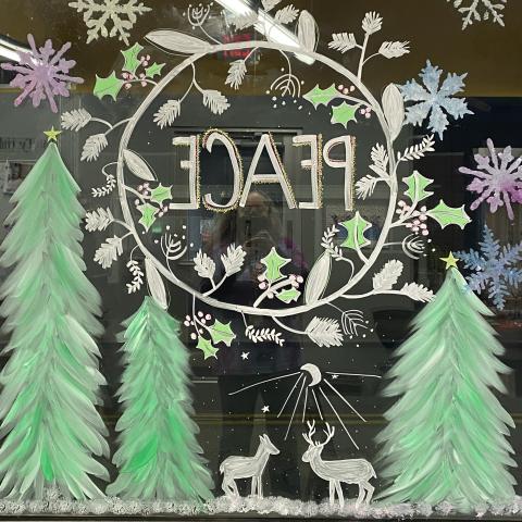 We are looking through a window with a wreath, the word "peace" and deer painted on it.