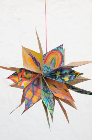 A star hangs from a string. It is constructed from brown, paper lunch bags that have been colored with patterns.