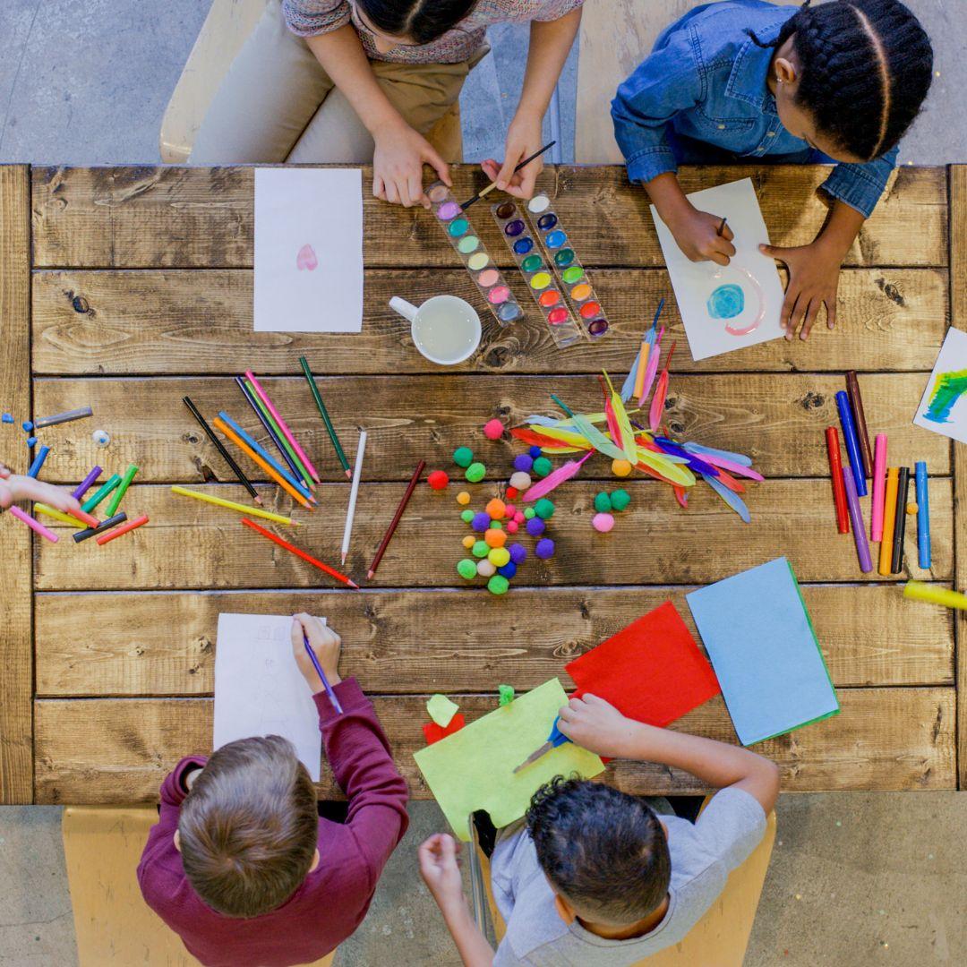 Children sit at a table with a variety of art supplies.