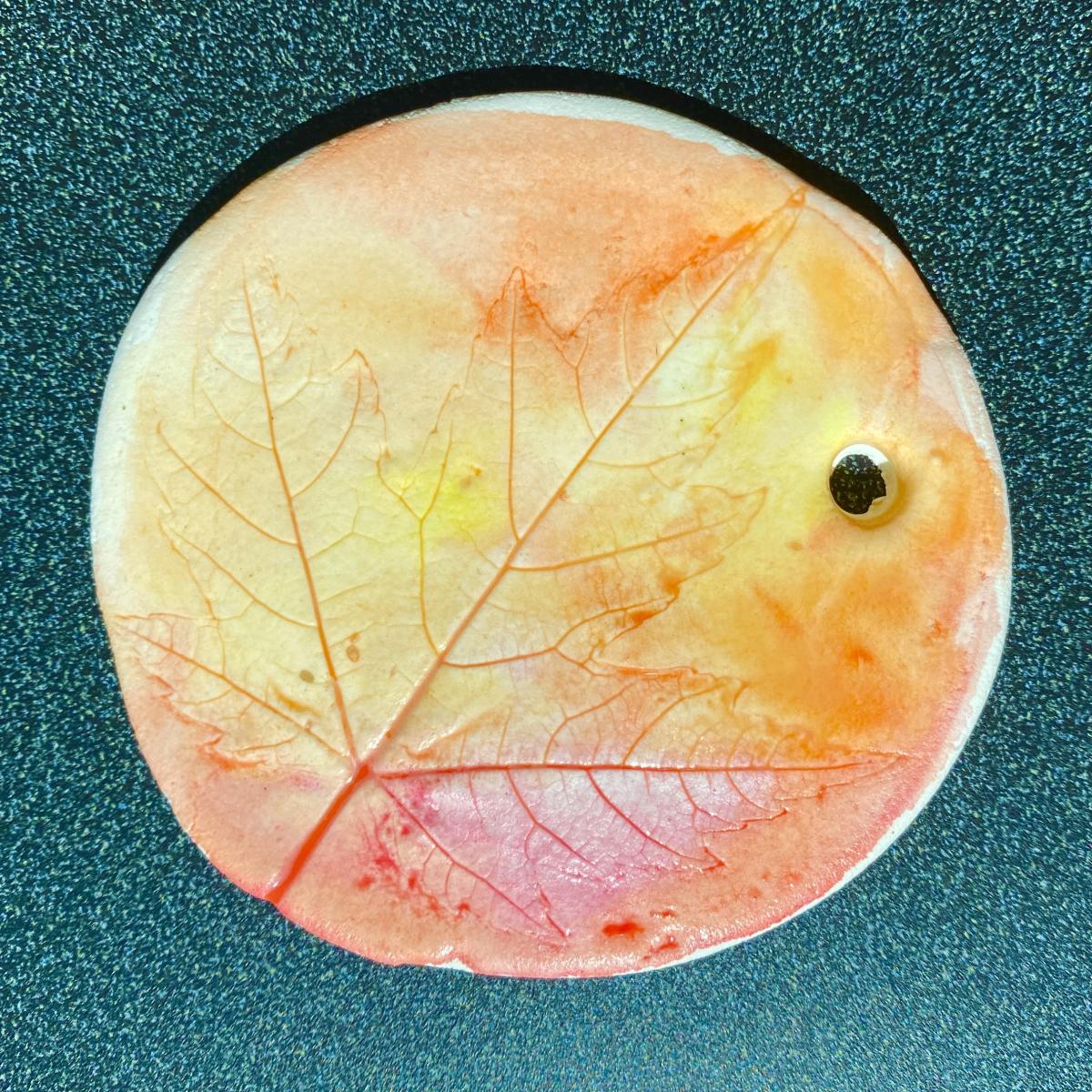 Clay medallion with leaf pressing painted a mix of red, orange, & yellow.