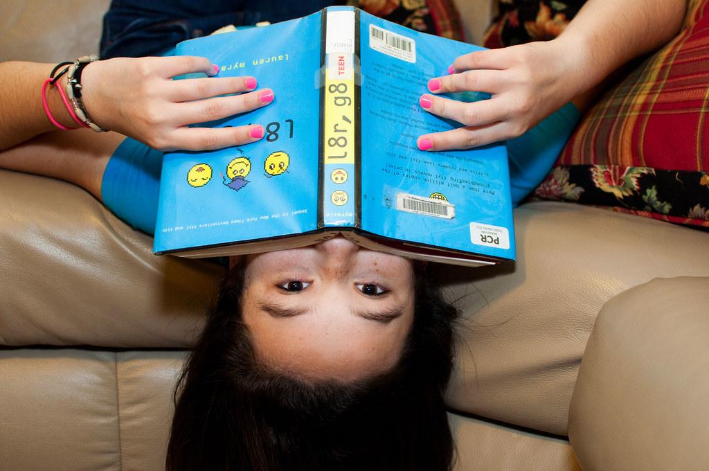 A teen reads a book while hanging upside down