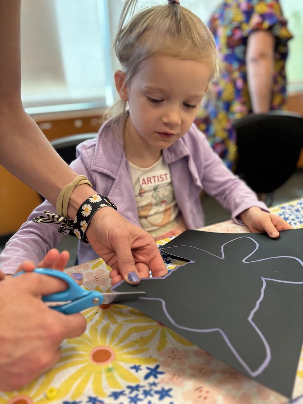 A mother's hands are seen cutting out a turtle while her little girl looks on.