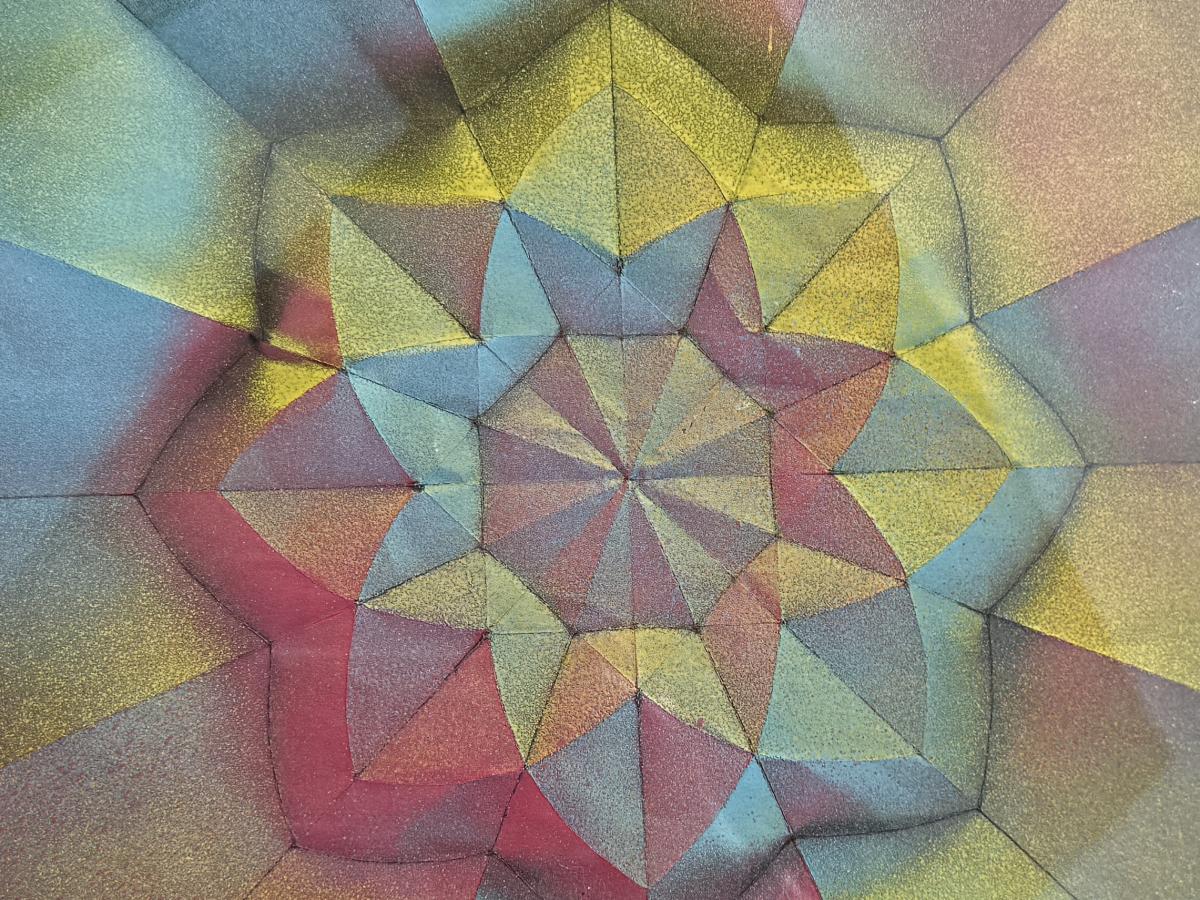 Spray painted paper folded and positioned into a rose window type pattern under glass