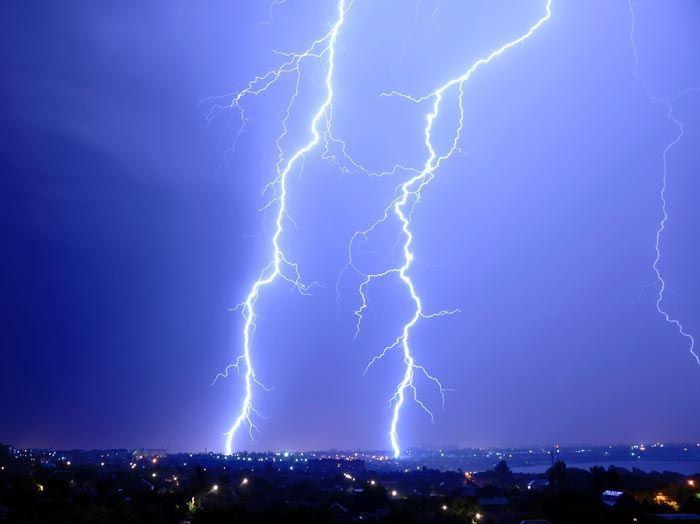 Two large lightening strikes hit the earth in a dark blue sky.