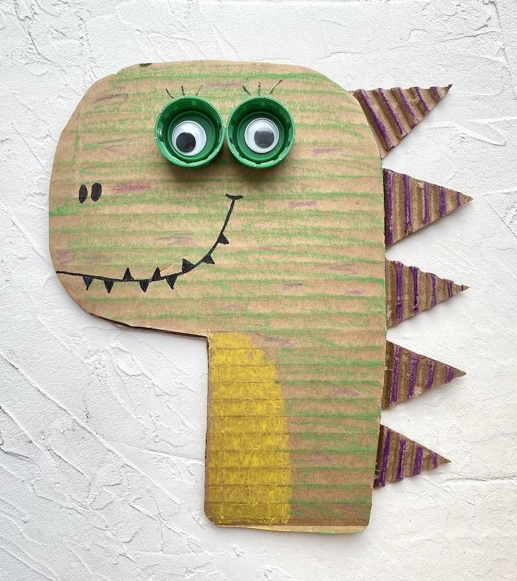 A dinosaur head created with cardboard, plastic caps and google eyes.