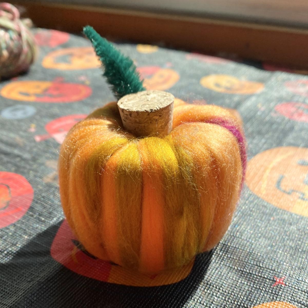 A photograph of a small pumpkin crafted out of wool roving, a pool noodle and a cork.