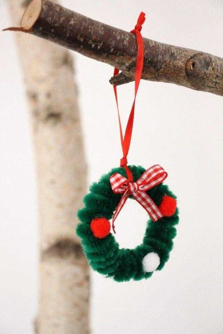 A small wreath hangs on a branch. It is made of pipe cleaners and pom poms.