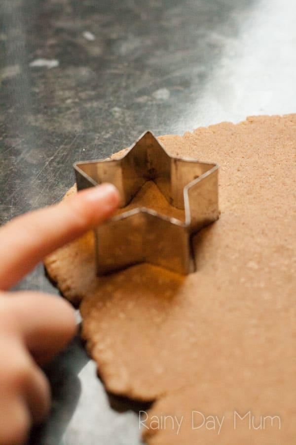 A child's finger pushes a star-shaped cookie cutter into brown dough.