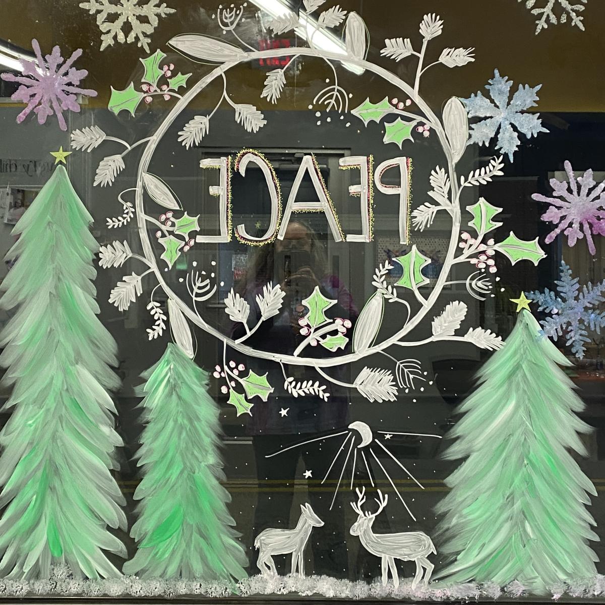 We are looking through a window with a wreath, the word "peace" and deer painted on it.